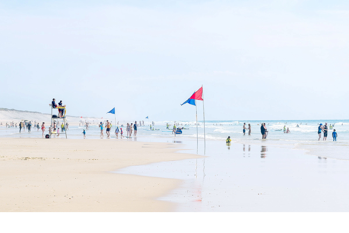 weitwinkliges Bild einer Strandszene: Menschen am baden, am plaudern und das vor der Weite des Meeres